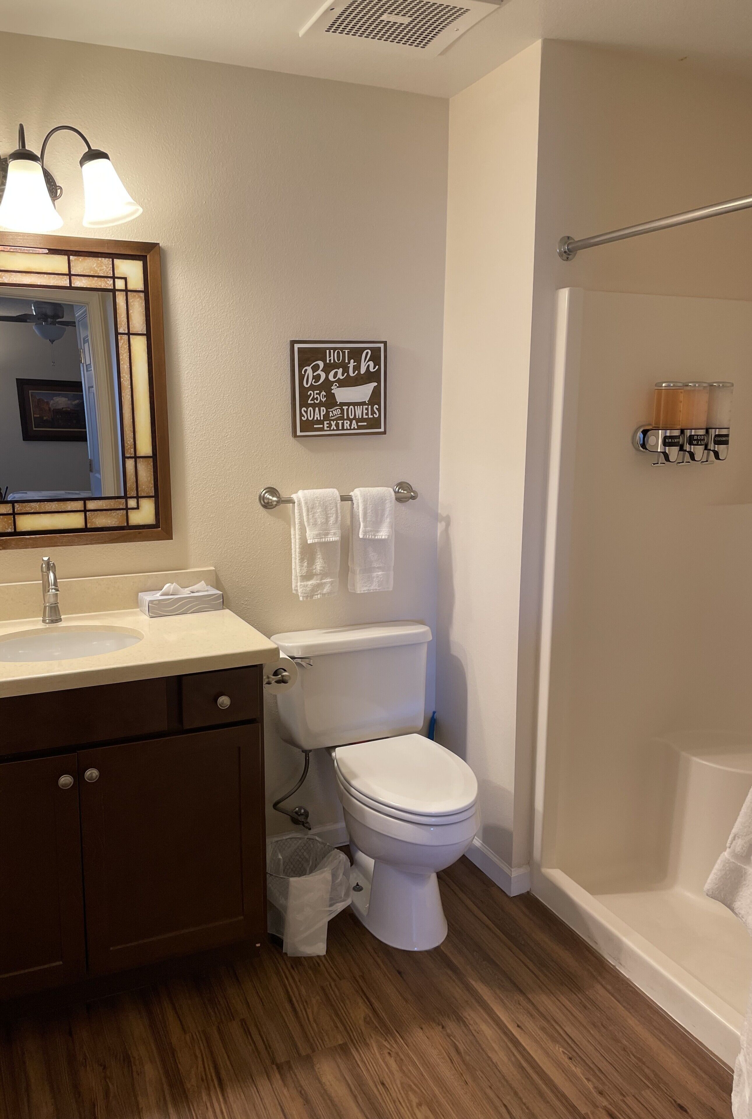 A bathroom with a sink, toilet, and shower. There is a sign above the toilet and a towel rack with towels.