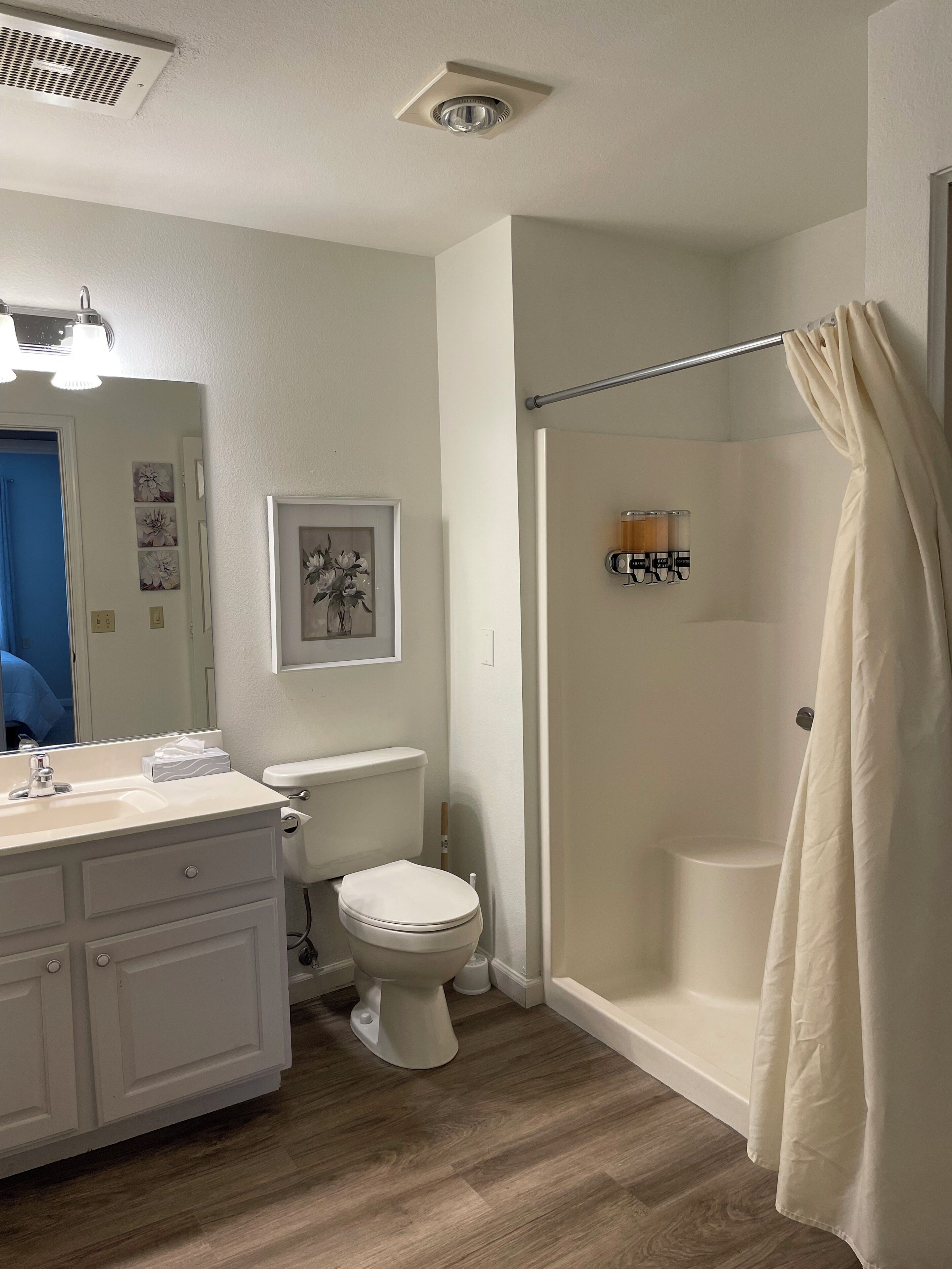 A bathroom with a toilet, sink, shower, and a mirror.