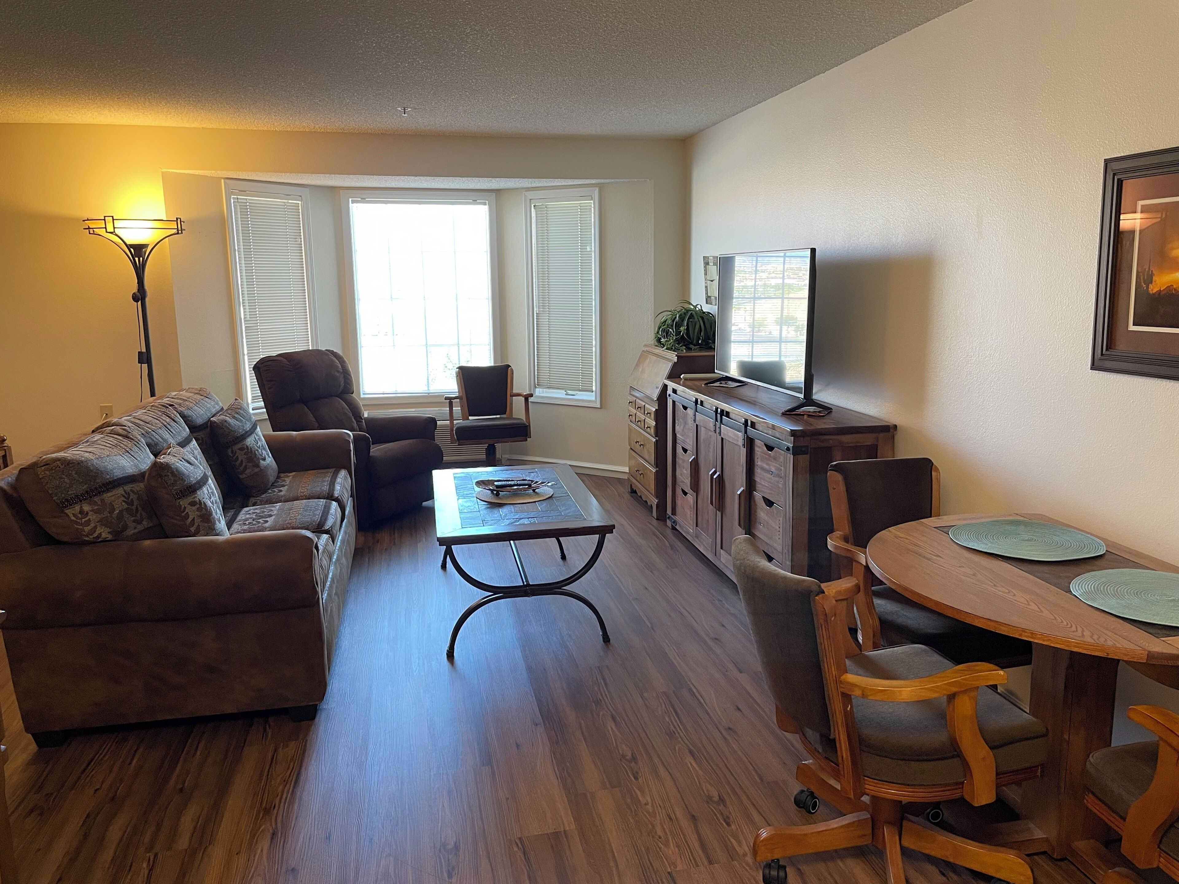 A living room with a sofa, armchair, coffee table, TV stand, and dining table.