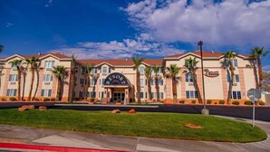A multi-story hotel with a prominent entrance, palm trees, and a clear blue sky. - Highland Estates Condotel (Mesquite)