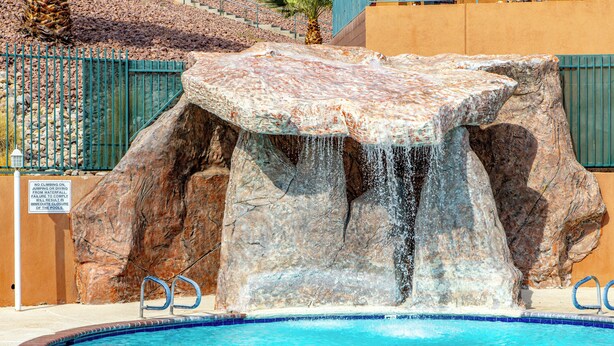 A pool with a waterfall feature, surrounded by rocks and a metal fence. - Highland Estates Condotel (Mesquite)