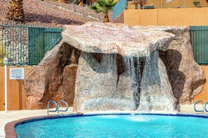 A pool with a waterfall feature, surrounded by rocks and a metal fence. - Highland Estates Condotel (Mesquite)