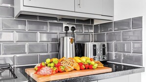 Une cuisine dotée d’un plan de travail en marbre, d’un grille-pain, d’une bouilloire et d’une planche à découper en bois sur laquelle sont disposés des fruits et des pâtisseries.