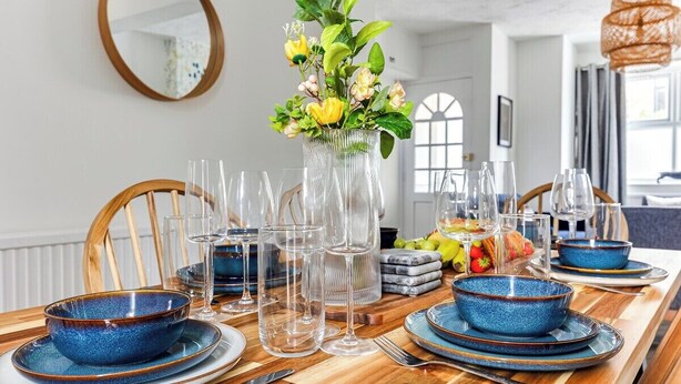 Une table à manger dressée avec des bols, des assiettes et des verres à vin transparents, le tout agrémenté d’un vase de fleurs.