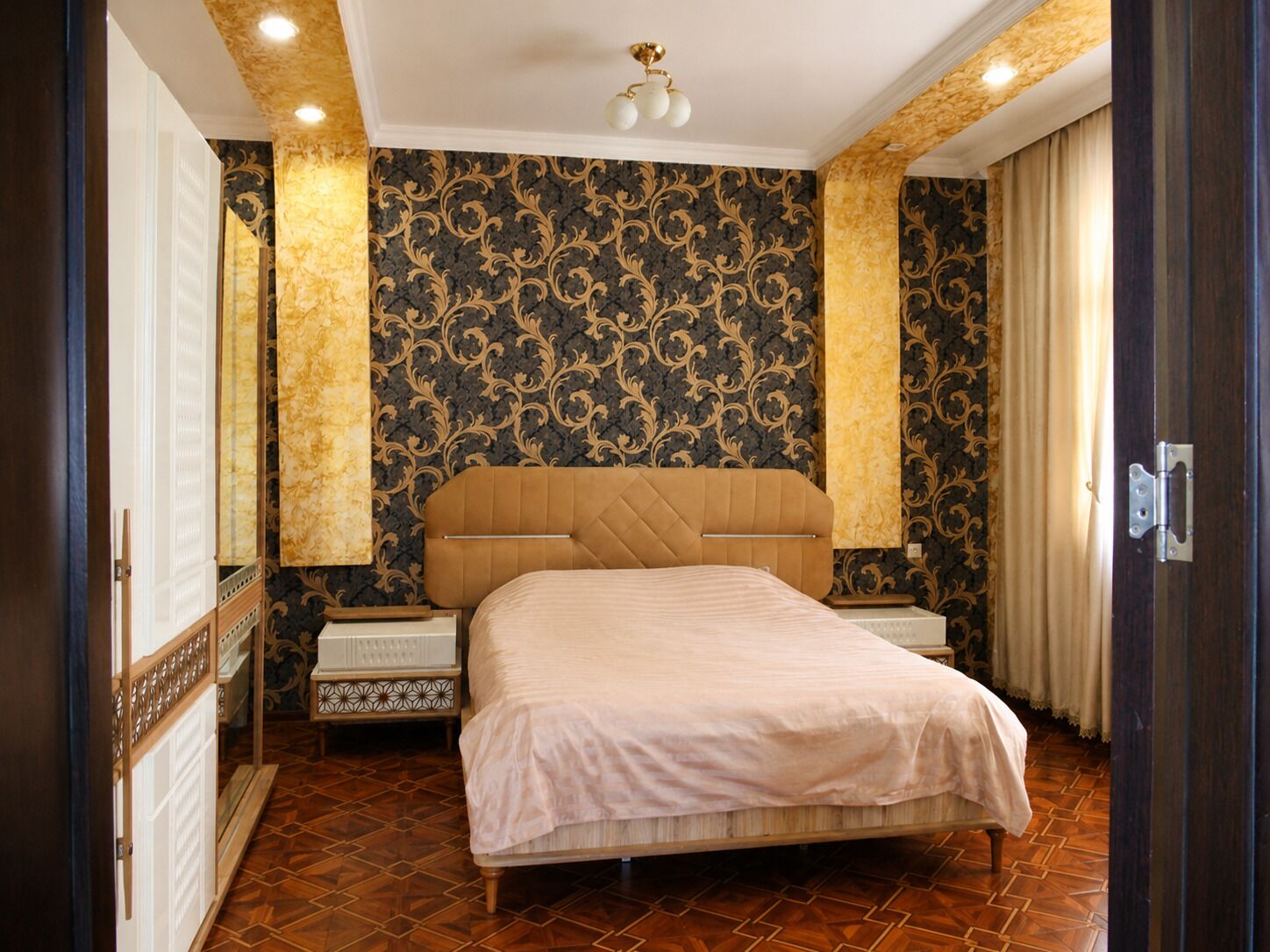 Une chambre à coucher avec un grand lit, une table de chevet, une commode et un papier peint à motifs.
