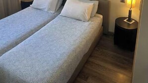 En dobbeltseng med to puder, et dekorativt vægophæng og to sengeborde med lamper.