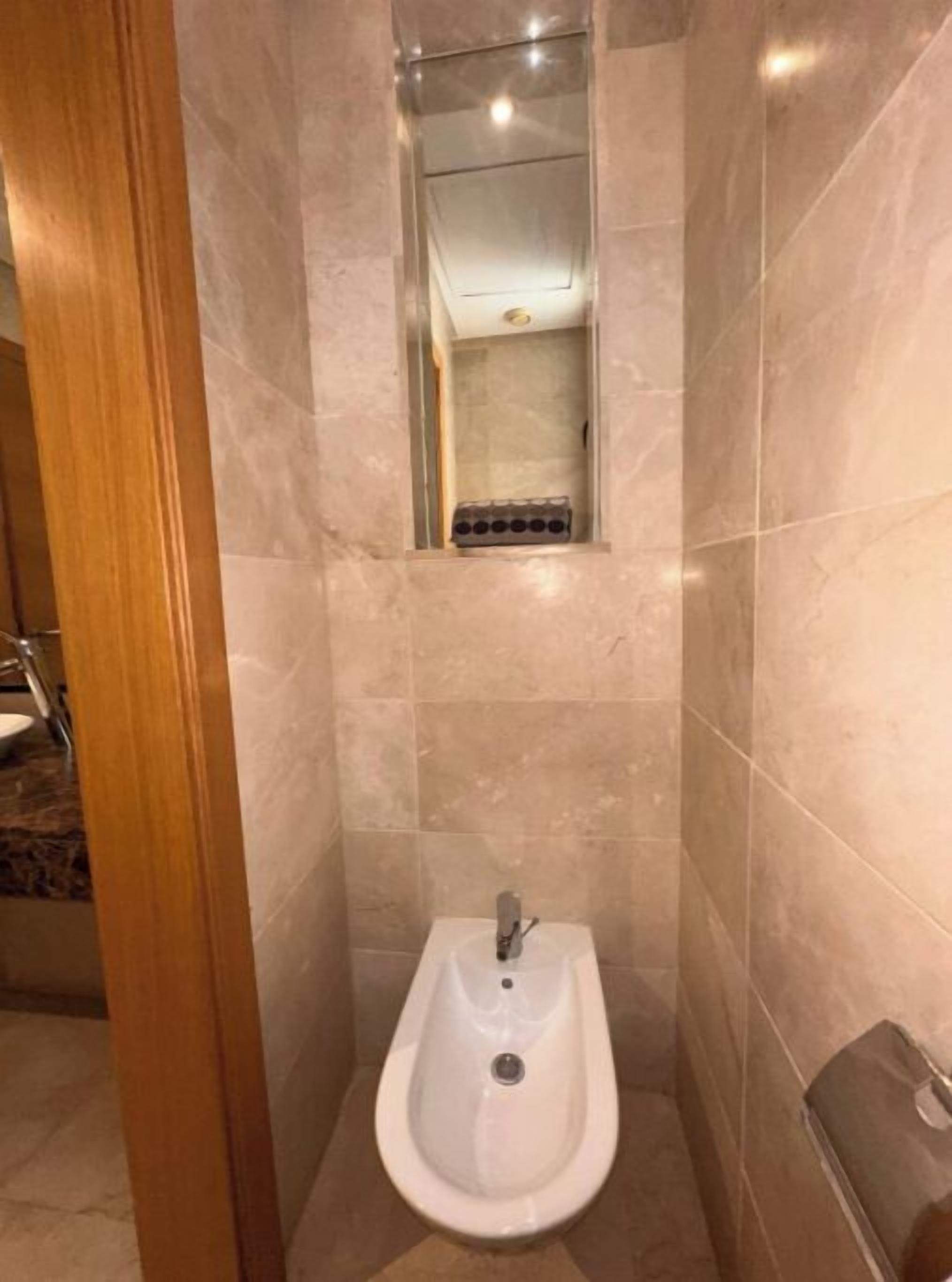 A small, modern bathroom with a pedestal sink, a mirror, and a shower area.