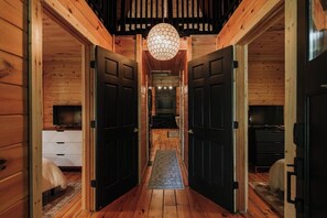 A wooden interior with a central hallway leading to a bedroom, a television in the room, and a hanging light fixture.