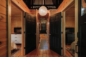 A wooden interior with a central hallway leading to a bedroom, a television in the room, and a hanging light fixture.