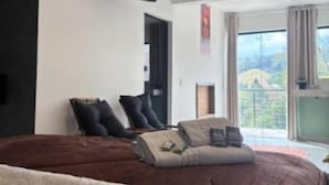 A bedroom with a large bed, a ceiling fan, a TV on the wall, and a window with a view of the outdoors. - Pousada Recanto da Cascata (Aguas de Lindoia)