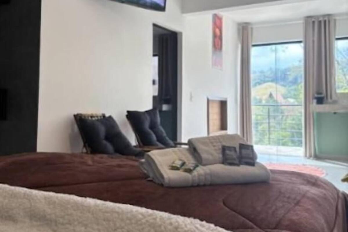 Un dormitorio con una cama grande, un ventilador de techo, un televisor en la pared y una ventana con vistas al exterior.
