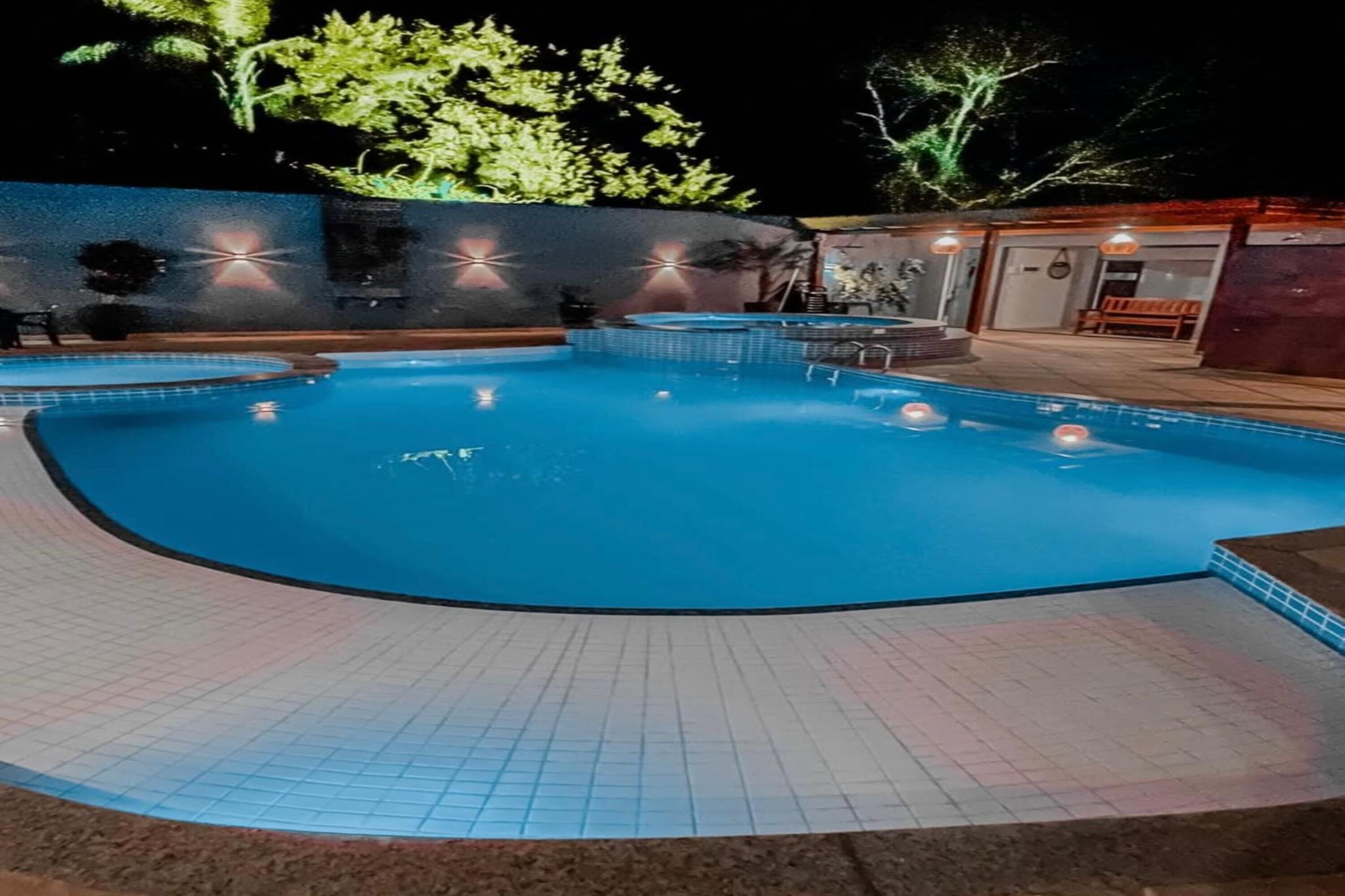 Una piscina con borde de baldosas, rodeada por un muro bajo y algunos árboles.