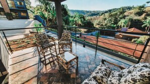 A balcony with a view of a hilly landscape, furnished with chairs and a sofa. - Pousada Recanto da Cascata (Aguas de Lindoia)