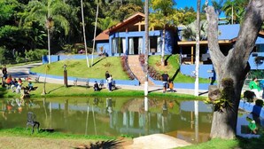 A building with a blue facade, a pond, and people around. - Pousada Recanto da Cascata (Aguas de Lindoia)