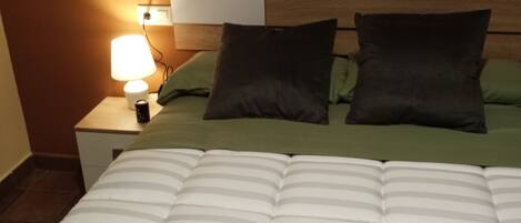 Una cama bien hecha con ropa de cama a rayas y dos almohadas, una lámpara de noche y un cabecero de madera.