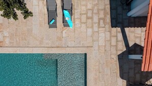 Vue aérienne d’un espace piscine avec deux chaises longues et une terrasse carrelée.