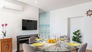 A modern dining area with a glass table, grey chairs, and a flat-screen TV mounted on the wall.