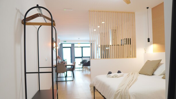 A modern hotel room with a bed, a wardrobe, a desk, and a chair.