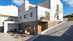 Ein modernes, zweistöckiges Haus mit Balkon, Naturstein-Fassade und gepflasterter Terrasse mit Gartenmöbeln und Blumentöpfen.