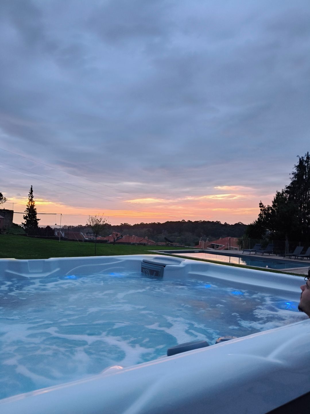 Boblebad med udsigt til en solnedgang og et græsareal med træer og bygninger i baggrunden.