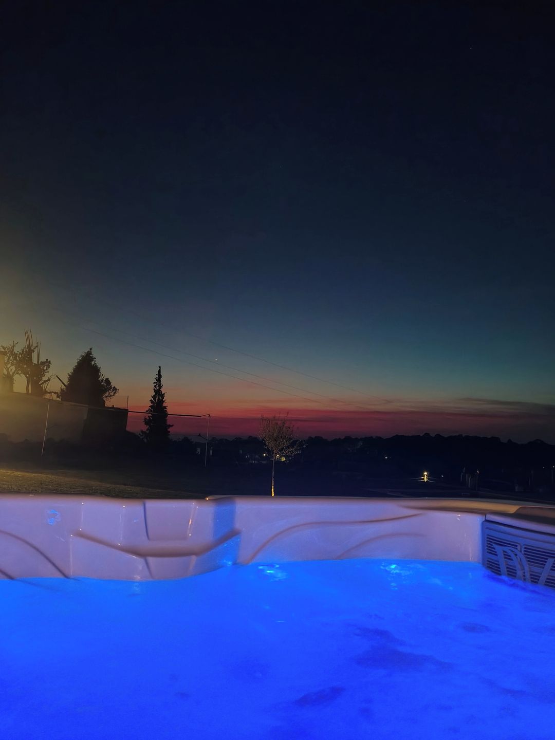 A hot tub with a view of a sunset over a residential area.