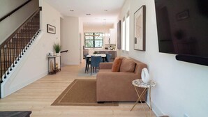 A modern living room with a staircase, a dining area, and a kitchen in the background.