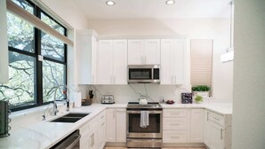 A modern kitchen with white cabinets, stainless steel appliances, a large window, and a view of trees.