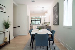 A modern dining area with a rectangular table, six chairs, and a potted plant.