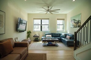 A living room with a brown sofa, a blue sofa, a coffee table, and a ceiling fan.