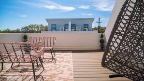 A balcony with wicker chairs, a patterned rug, and a view of a modern building.