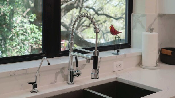 A kitchen with a double sink, a window with a view of trees, and a bird decoration on the windowsill.