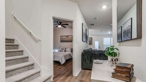 A staircase leading to a bedroom with a ceiling fan, a bedside table with books, and a plant.