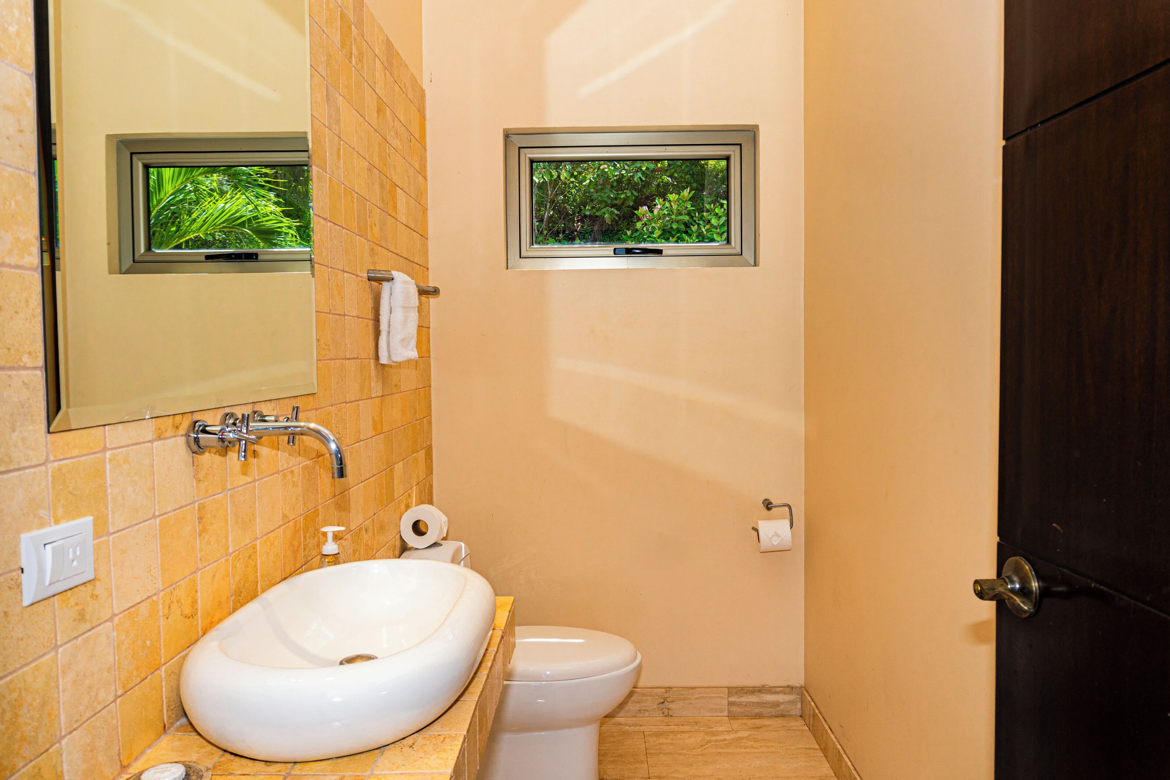 Un baño con lavamanos, inodoro y dos ventanas.