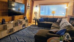 Un salón acogedor con una amplia televisión de pantalla plana, estanterías de madera, un sofá modular y una alfombra estampada.