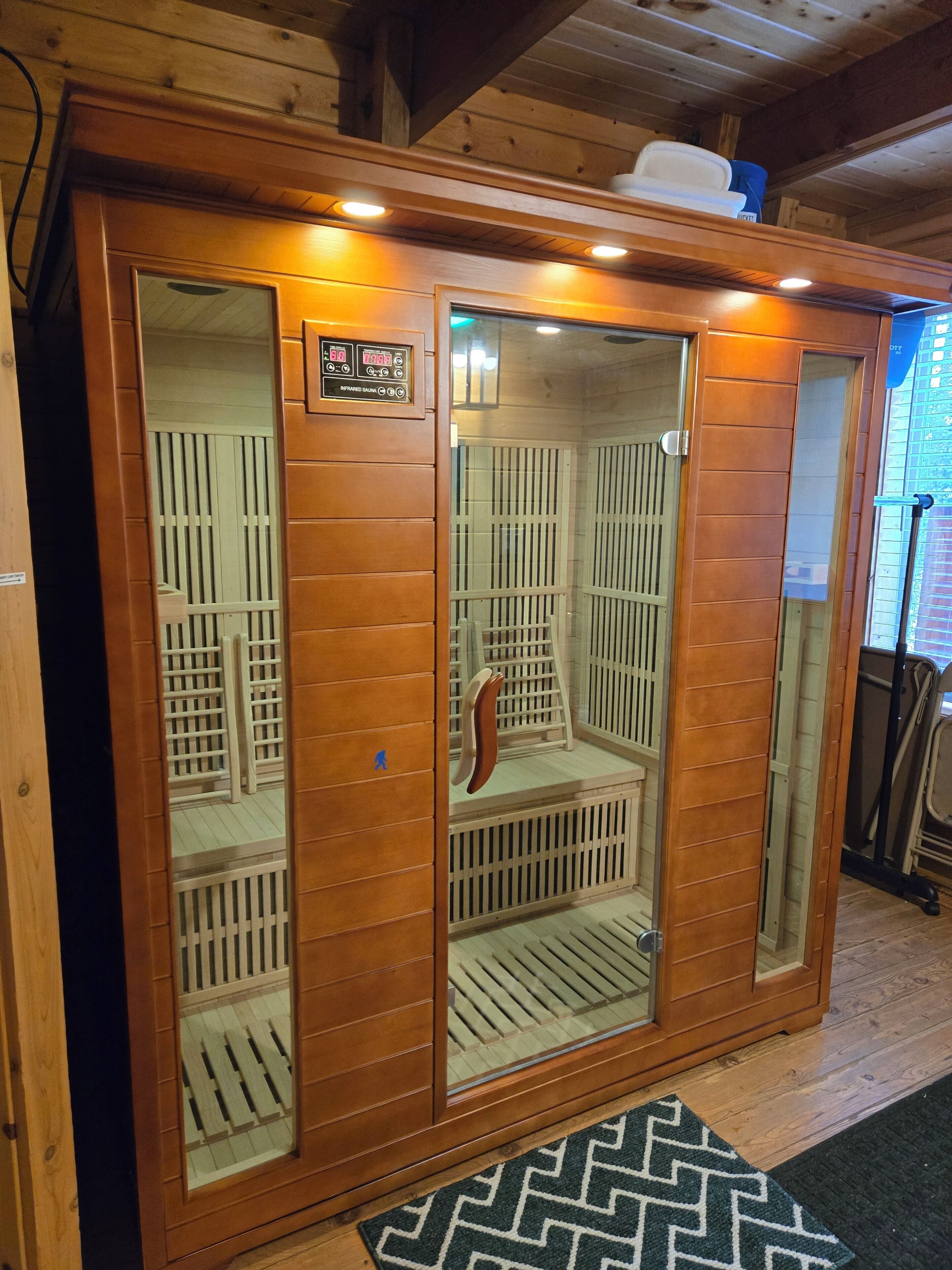 Een sauna met houten wanden en een glazen deur, met een bedieningspaneel en een bankje binnen.