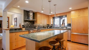 Uma cozinha moderna com armários de madeira, uma ilha grande com banquetas, eletrodomésticos de aço inoxidável e iluminação pendente.