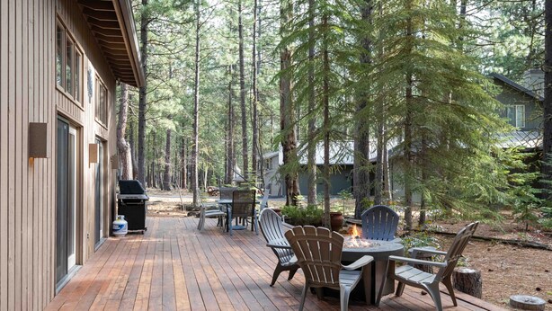 Um deck de madeira com móveis externos e churrasqueira, cercado por árvores altas.