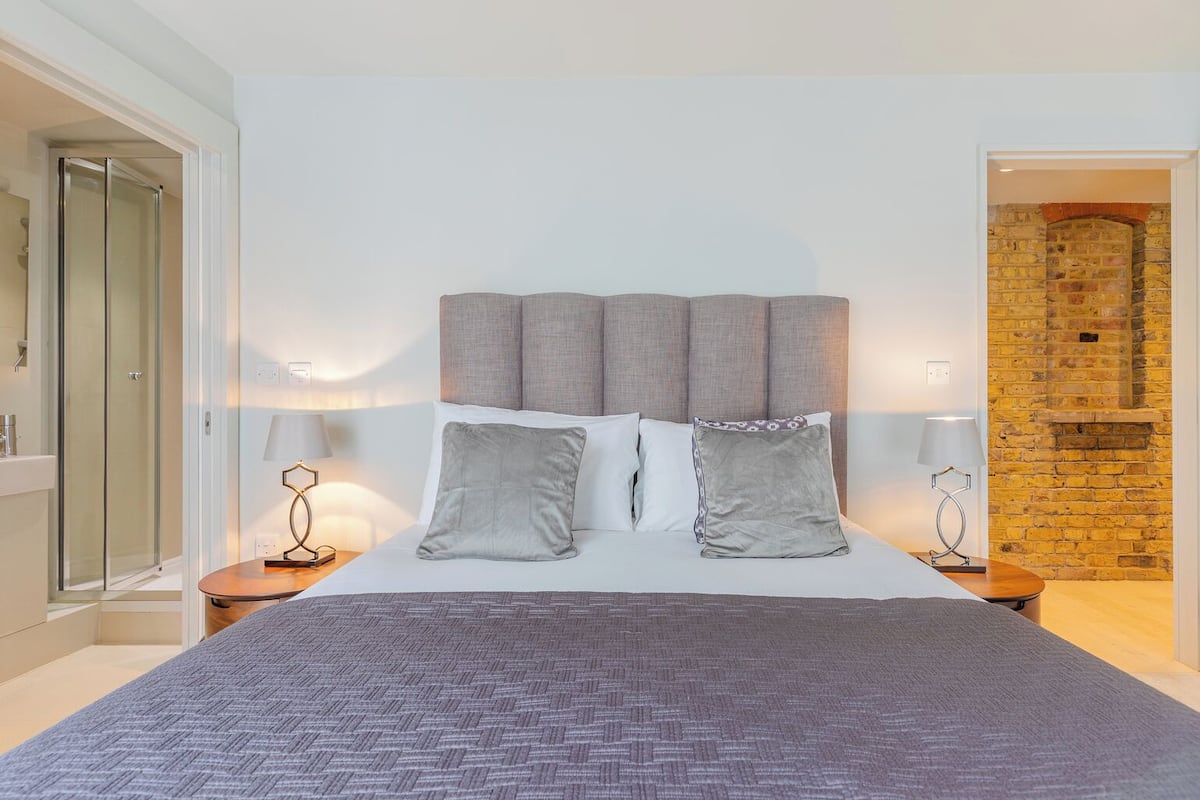 A modern bedroom with a large bed, two bedside tables, a headboard, and a brick wall.