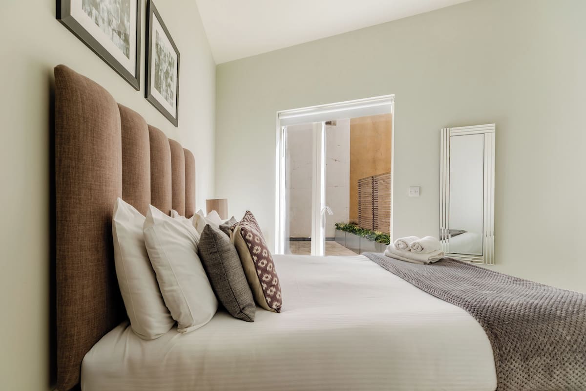 A neatly made bed with a headboard, a large mirror, and a door leading to a balcony.