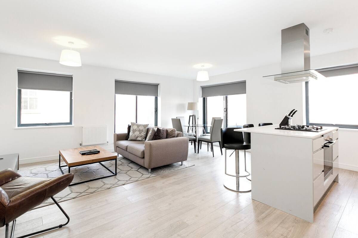 A modern living room with a sofa, coffee table, and a small kitchen area with a stove.