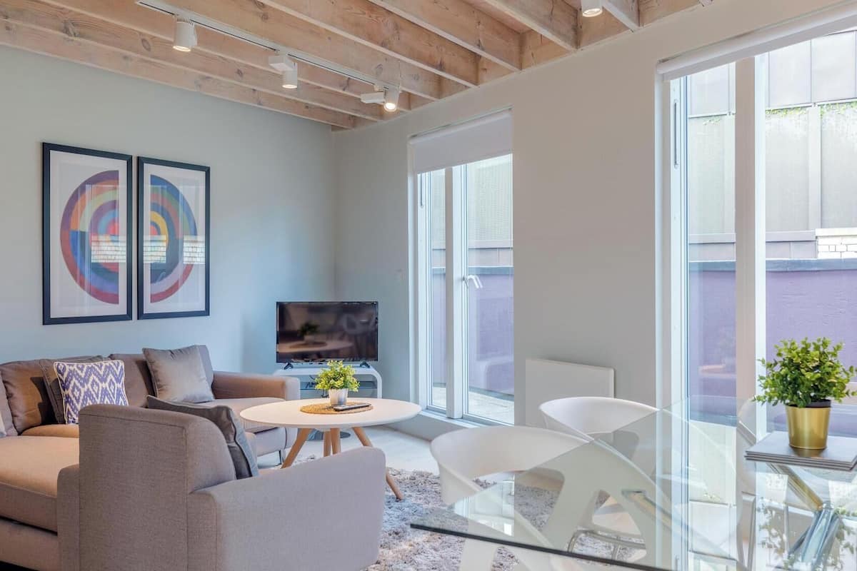 A modern living room with a sofa, a coffee table, and a TV. There are two framed artworks on the wall and a potted plant on a table.