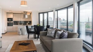 A modern apartment with a kitchen, dining area, and a large window offering a city view. - Excel Apartments Ltd (Bromley)