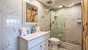 Un baño moderno con baldosas de mármol, un mueble de tocador de madera, una cabina de ducha de vidrio y un inodoro.