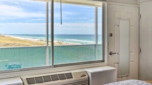 Una habitación con un ventanal grande con vista a la playa, una puerta blanca y un equipo de aire acondicionado instalado.