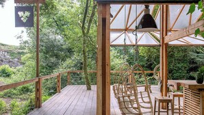Eine Holzterrasse mit einem Holzschaukelstuhl und einer Hängelampe, umgeben von üppigem Grün.