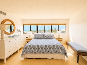 A bedroom with a bed, bedside tables, a mirror, and a view of the ocean.