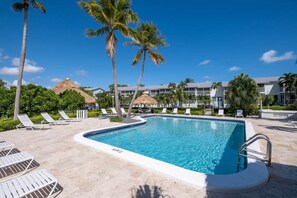 A pool area with lounge chairs, palm trees, and a building with a thatched roof in the background.