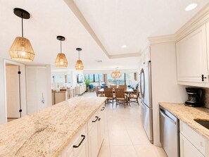 A modern kitchen with a marble countertop, stainless steel appliances, and pendant lighting.