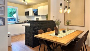 Una cocina moderna con una isla central, un comedor con una mesa y sillas de madera, y una obra de arte grande en la pared.