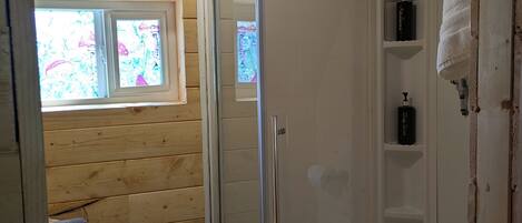 A wooden cabin bathroom with a glass-enclosed shower, a toilet, and a window with a view.